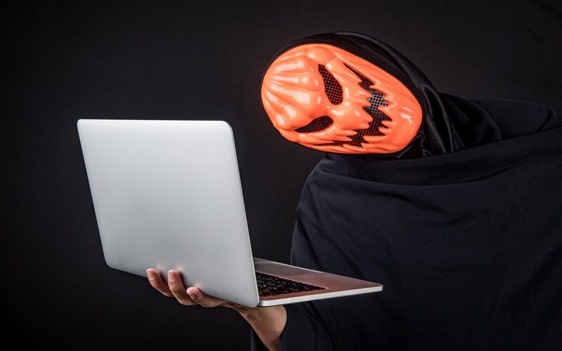 Guy wearing pumpkin mask holding a laptop