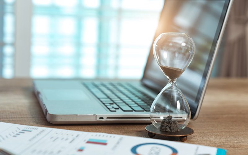 Hour glass with sand next to a laptop