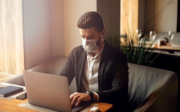 Man using protective face mask while working on laptop